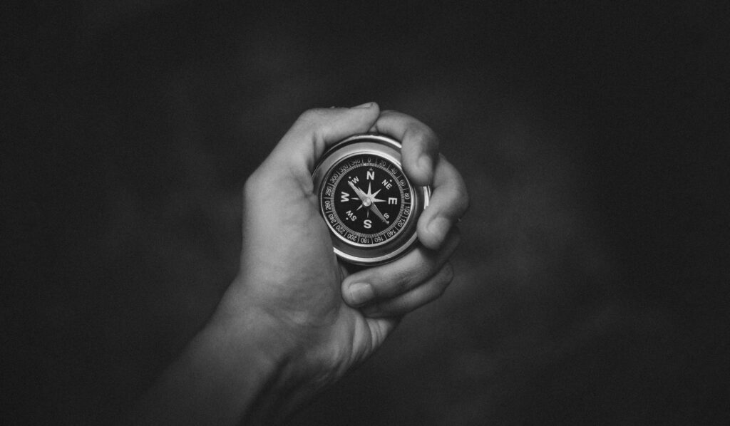Home A black and white close-up of a hand holding a compass, symbolizing exploration.