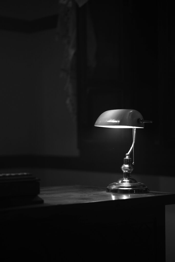 A classic desk lamp illuminates a table in a dimly lit room, creating a moody atmosphere.